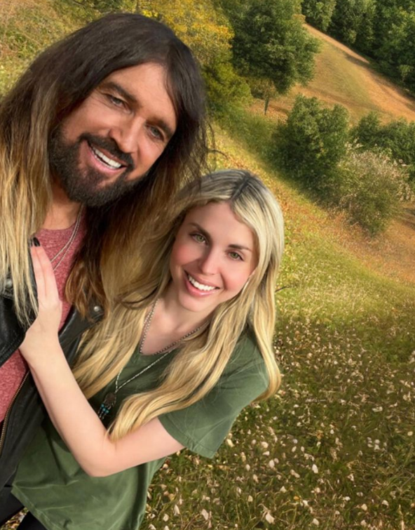 Billy Ray Cyrus and Firerose. They are smiling.